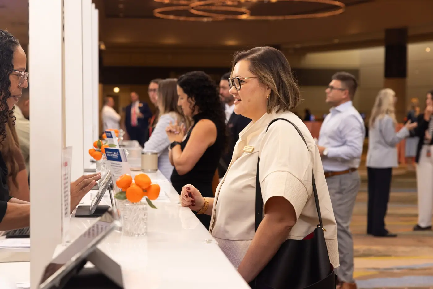 An attendee speaks with staff at a registration counter while other guests gather nearby.
