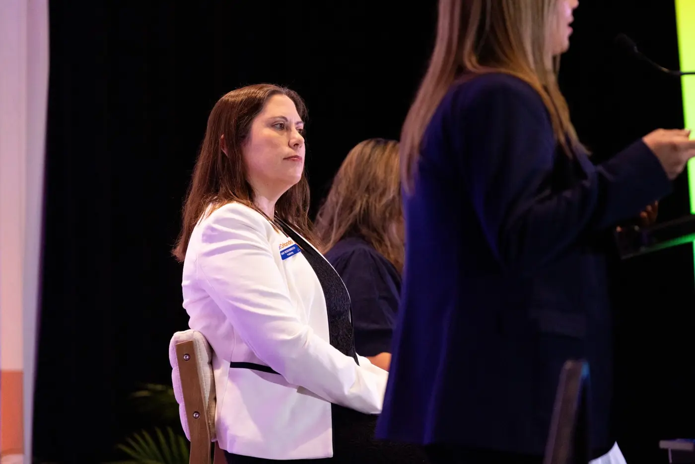 A seated panelist smiles while a standing speaker addresses the room.