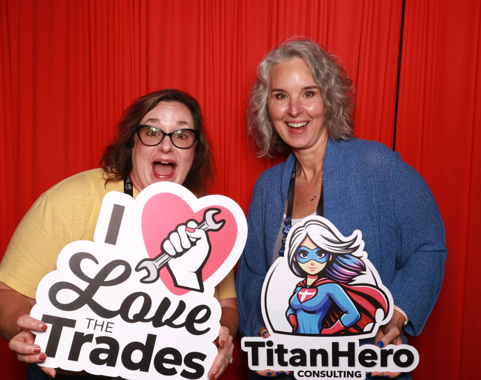 Two Lady Titans guests posing with Love the Trades and TitanHero Consulting props