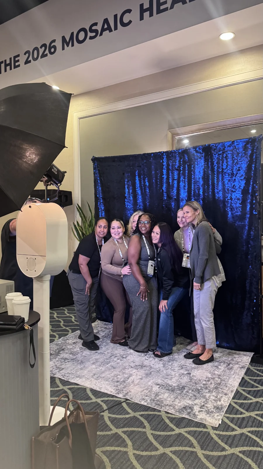 Mosaic Health retreat guests posing together in front of the blue photo booth backdrop