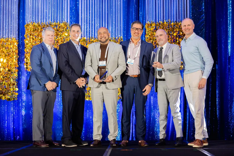 Awards photography of honorees on stage with a trophy in front of a gold backdrop at a corporate gala
