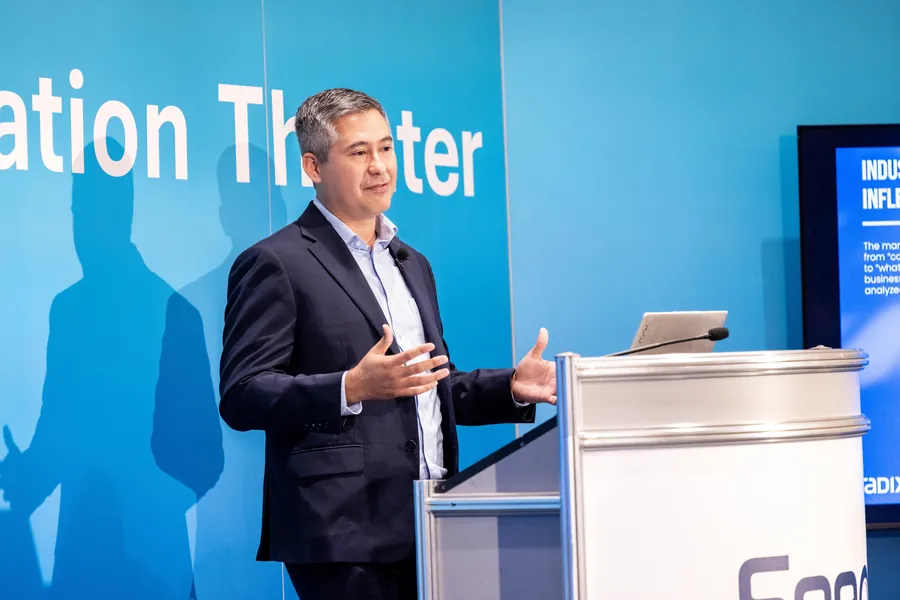 Conference photography of a speaker at a podium in front of a branded session theater screen