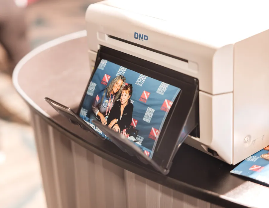On-site printing add-on dispensing a branded step-and-repeat print for a guest takeaway at a corporate event