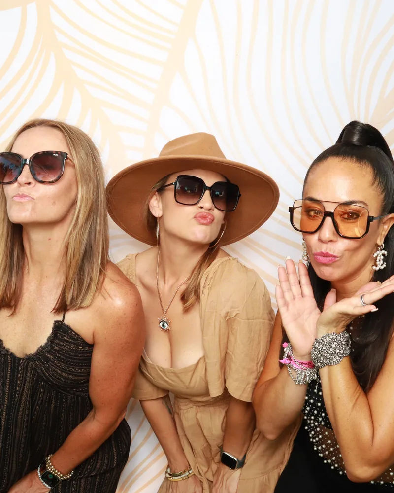 Three guests posing in festival style at a gold palm-leaf backdrop in an Orlando photo booth