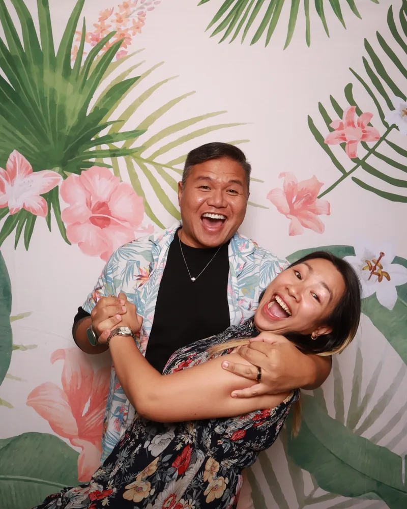 Couple laughing together at a tropical floral backdrop in an Orlando Pro DSLR photo booth