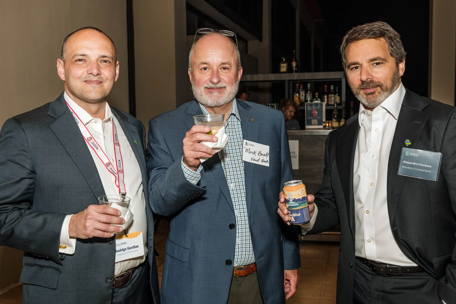 Roaming photograph of three corporate guests with name badges holding drinks at a reception bar