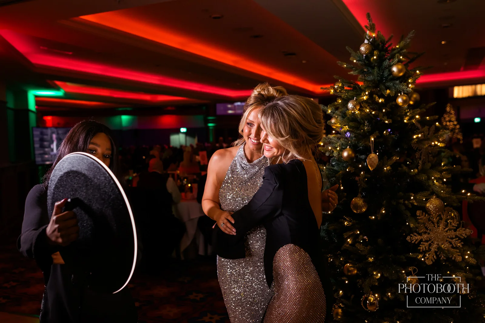 Two guests sharing a candid moment beside a roaming photo booth ring light at a corporate holiday gala