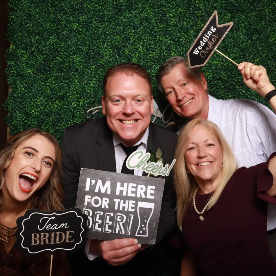 Wedding guests with fun signs and props at a Central Florida photo booth on a greenery backdrop